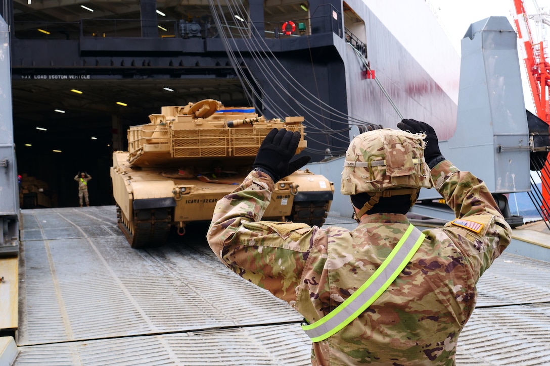 A soldier guides a tank onto a ship