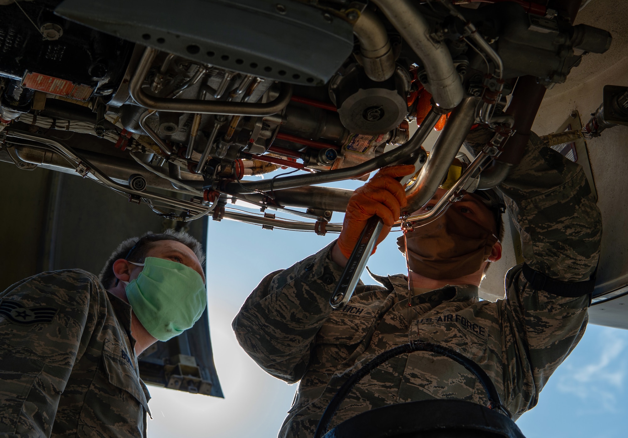 Staff Sgt. Christopher Bowen, 62nd Maintenance Squadron (MXS) hydraulics technician, supervises while Airman 1st Class Ian Cernetich, 62nd MXS hydraulics apprentice, works to remove a hydraulic pump from the engine of a C-17 Globemaster III at Joint Base Lewis-McChord, Wash., April 14, 2020. Both Airmen are wearing protective masks to help stop the spread of COVID-19 while they work. (U.S. Air Force photo by Senior Airman Tryphena Mayhugh)