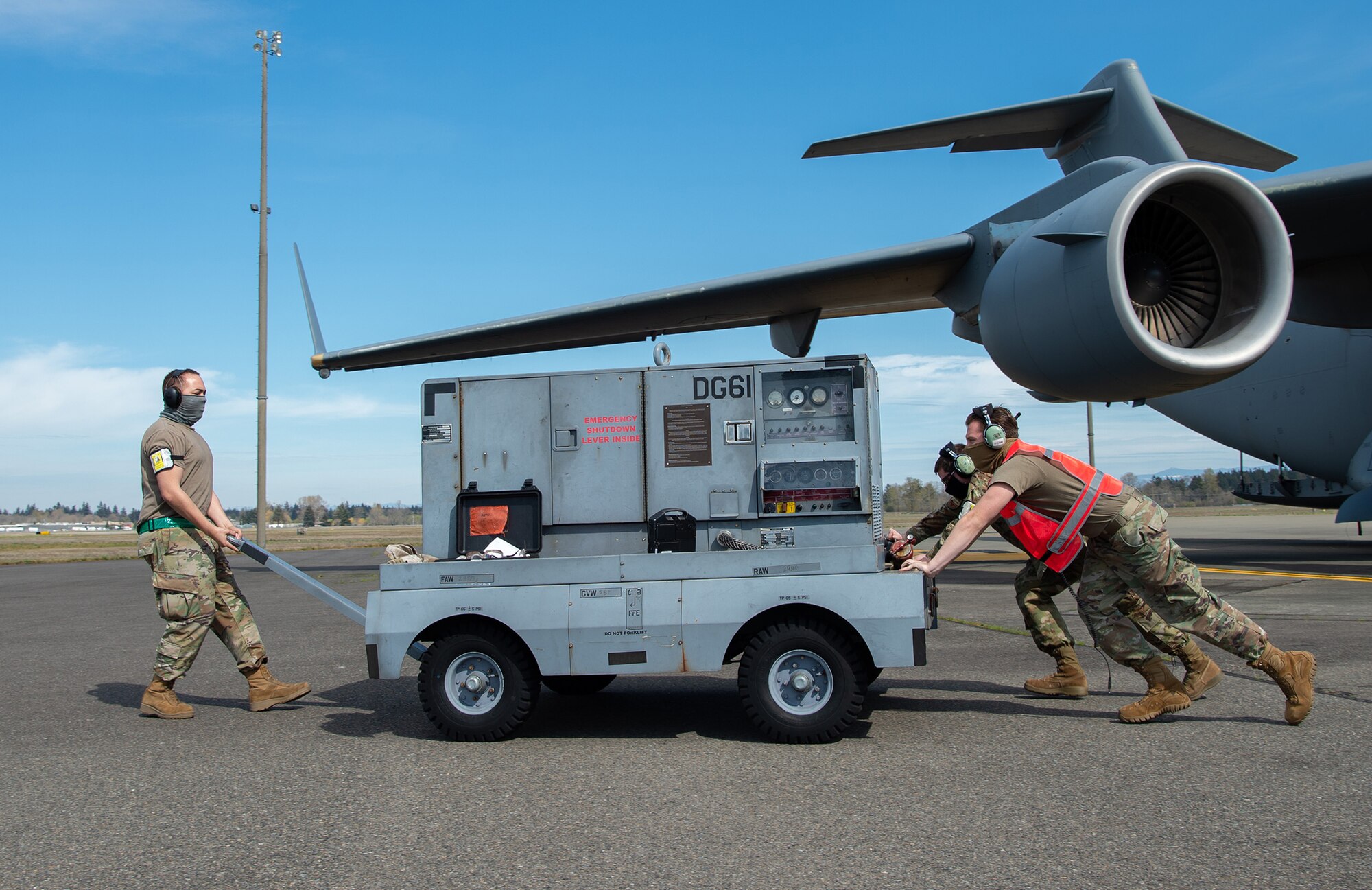 Tech. Sgt. Veryon Moore, 62nd Aircraft Maintenance Squadron (AMXS) integrated flight control systems craftsman; Senior Airman Tyler DiNoto, 62nd AMXS integrated flight control systems journeyman, front right; and Staff Sgt. Bertrand Foley, 62nd AMXS communication, navigation and mission systems craftsman, move a generator away from a C-17 Globemaster III at Joint Base Lewis-McChord, Wash., April 14, 2020. Airmen wear protective masks to protect themselves and others from the spread of COVID-19 while continuing to perform their duties. (U.S. Air Force photo by Senior Airman Tryphena Mayhugh)