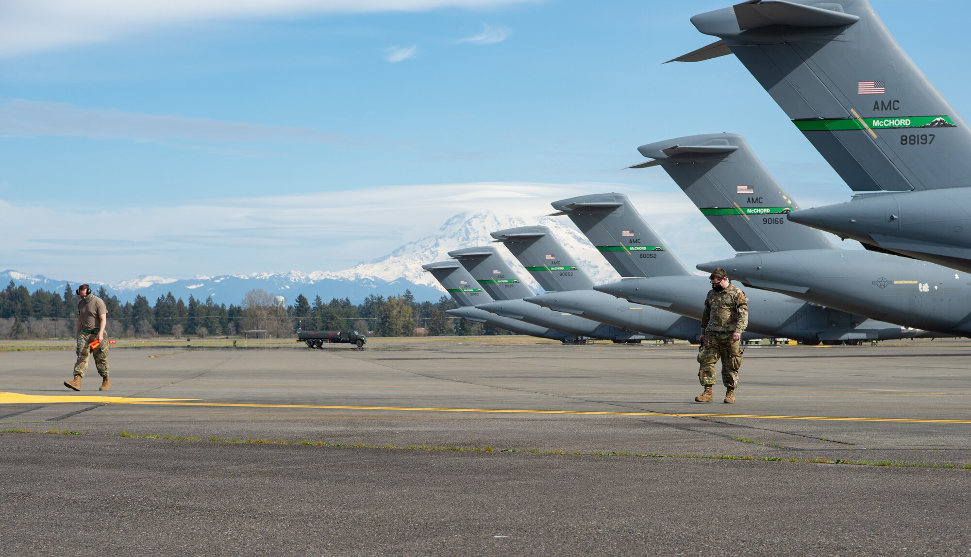 Tech. Sgt. Veryon Moore, 62nd Aircraft Maintenance Squadron (AMXS) integrated flight control systems craftsman, left, and Staff Sgt. Bertrand Foley, 62nd AMXS communication, navigation and mission systems craftsman, search for foreign objects or debris after a C-17 Globemaster III departed from the flightline at Joint Base Lewis-McChord, Wash., April 14, 2020. The Airmen are maintaining at least six feet apart and wearing protective masks to help slow the spread of COVID-19 while continuing to execute their mission. (U.S. Air Force photo by Senior Airman Tryphena Mayhugh)