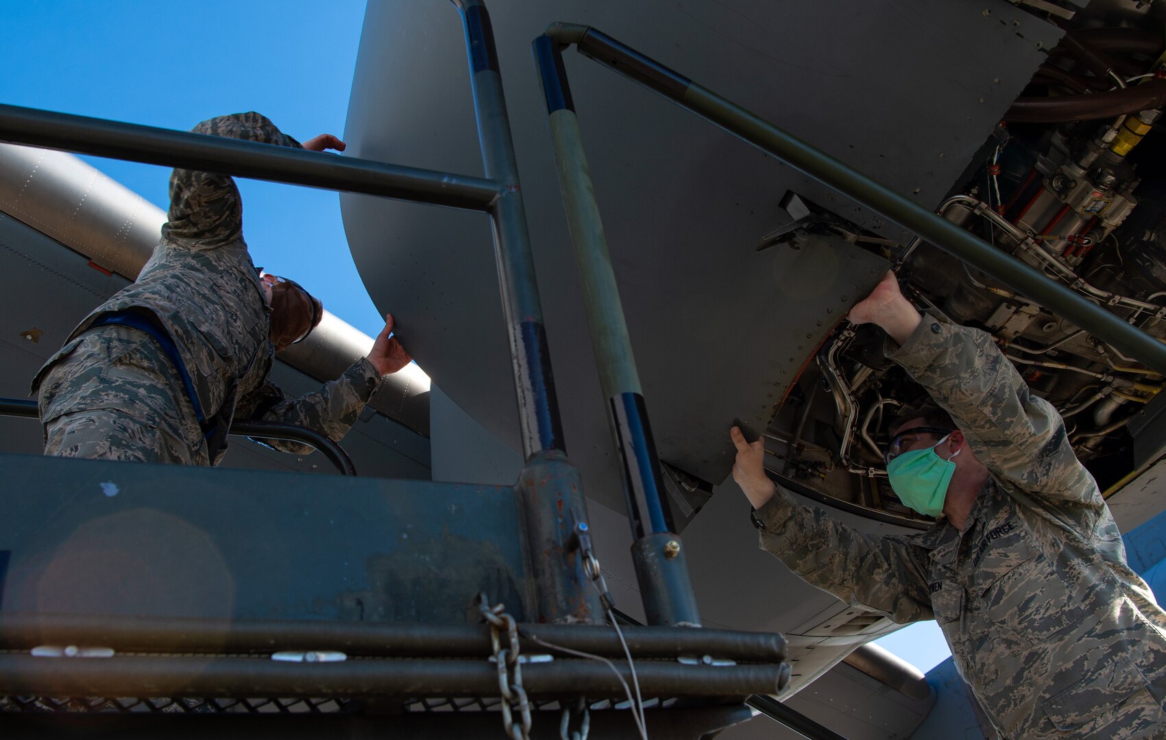 Staff Sgt. Christopher Bowen, 62nd Maintenance Squadron (MXS) hydraulics technician, right, and Airman 1st Class Ian Cernetich, 62nd MXS hydraulics apprentice, open the panel covering the engine of a C-17 Globemaster III at Joint Base Lewis-McChord, Wash., April 14, 2020. Maintenance Airmen are mission essential and cannot be sent home to maintain social distancing during the COVID-19 pandemic, so they must take precautions such as wearing protective masks to stay healthy while continuing to execute their mission. (U.S. Air Force photo by Senior Airman Tryphena Mayhugh)