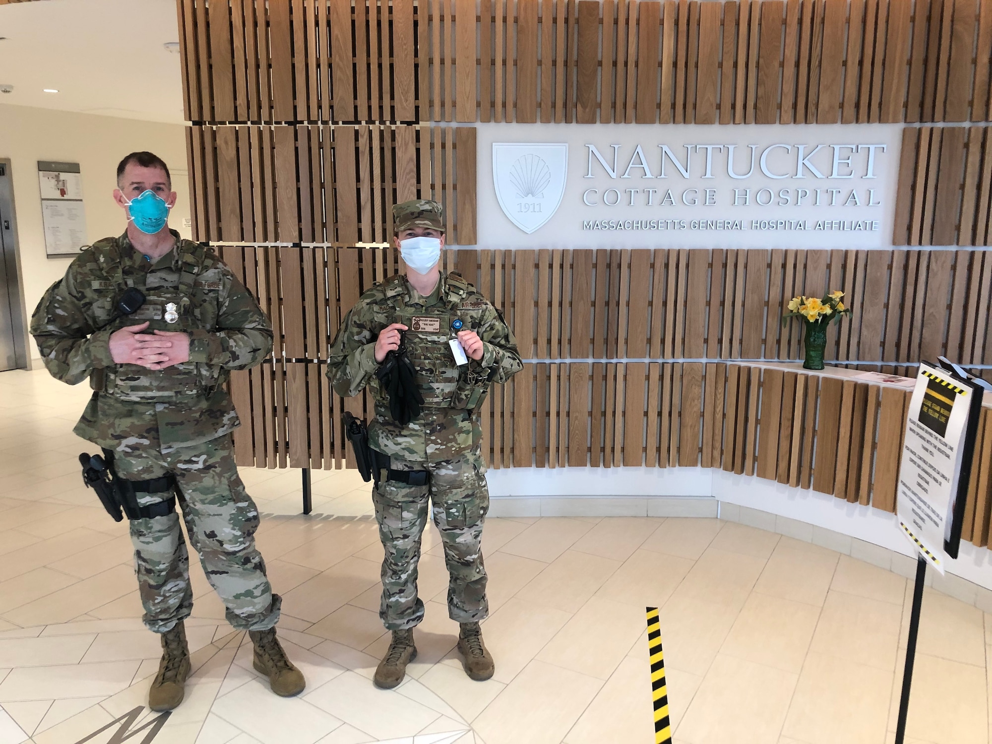 Two security forces defenders wearing face masks stand at the entrance to Nantucket Cottage Hospital