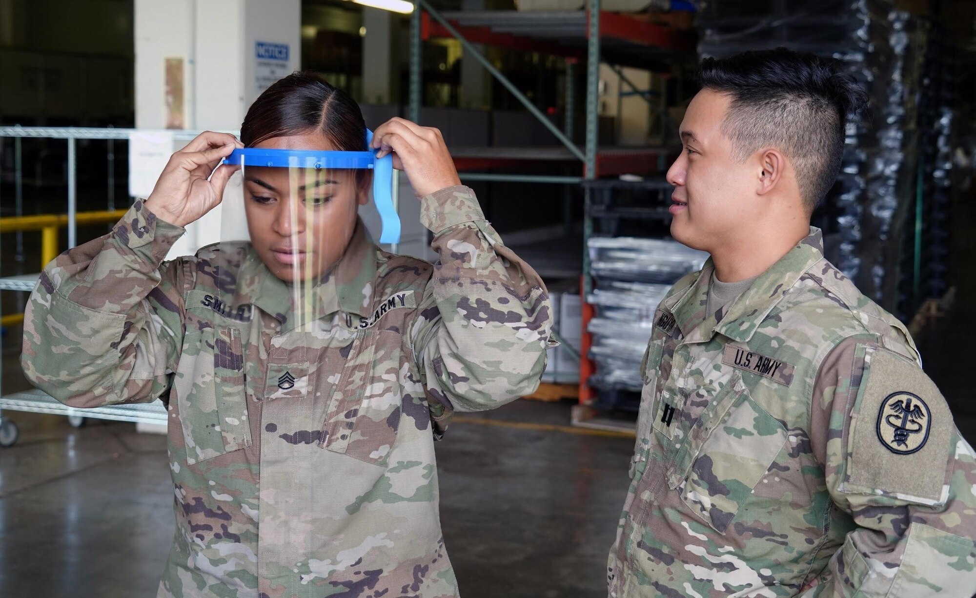 U.S. Army Staff Sgt. Jacklyn Smith, Tripler Army Medical Center medical warehouse non-commissioned officer in charge, receives assistance from U.S. Army Capt. Scott Nguyen, TAMC General Surgery resident physician, with adjusting her face shield at TAMC, Hawaii, April 3, 2020. Due to a shortage of disposable masks, the 15th Wing is using 3D printers to make face shields to donate across the island to combat the COVID-19 pandemic.  (U.S. Air Force photo by Airman 1st Class Erin Baxter)