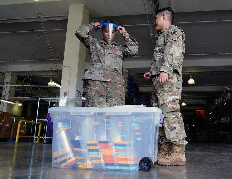 U.S Army Staff Sgt. Jacklyn Smith, Tripler Army Medical Center medical warehouse non-commissioned officer in charge, receives assistance from U.S. Army Capt. Scott Nguyen, TAMC General Surgery resident physician, with adjusting her face shield at TAMC, Hawaii, April 3, 2020. Due to a shortage of disposable masks, the 15th Wing is using 3D printers to make face shields to donate across the island to combat the COVID-19 pandemic.  (U.S. Air Force photo by Airman 1st Class Erin Baxter)