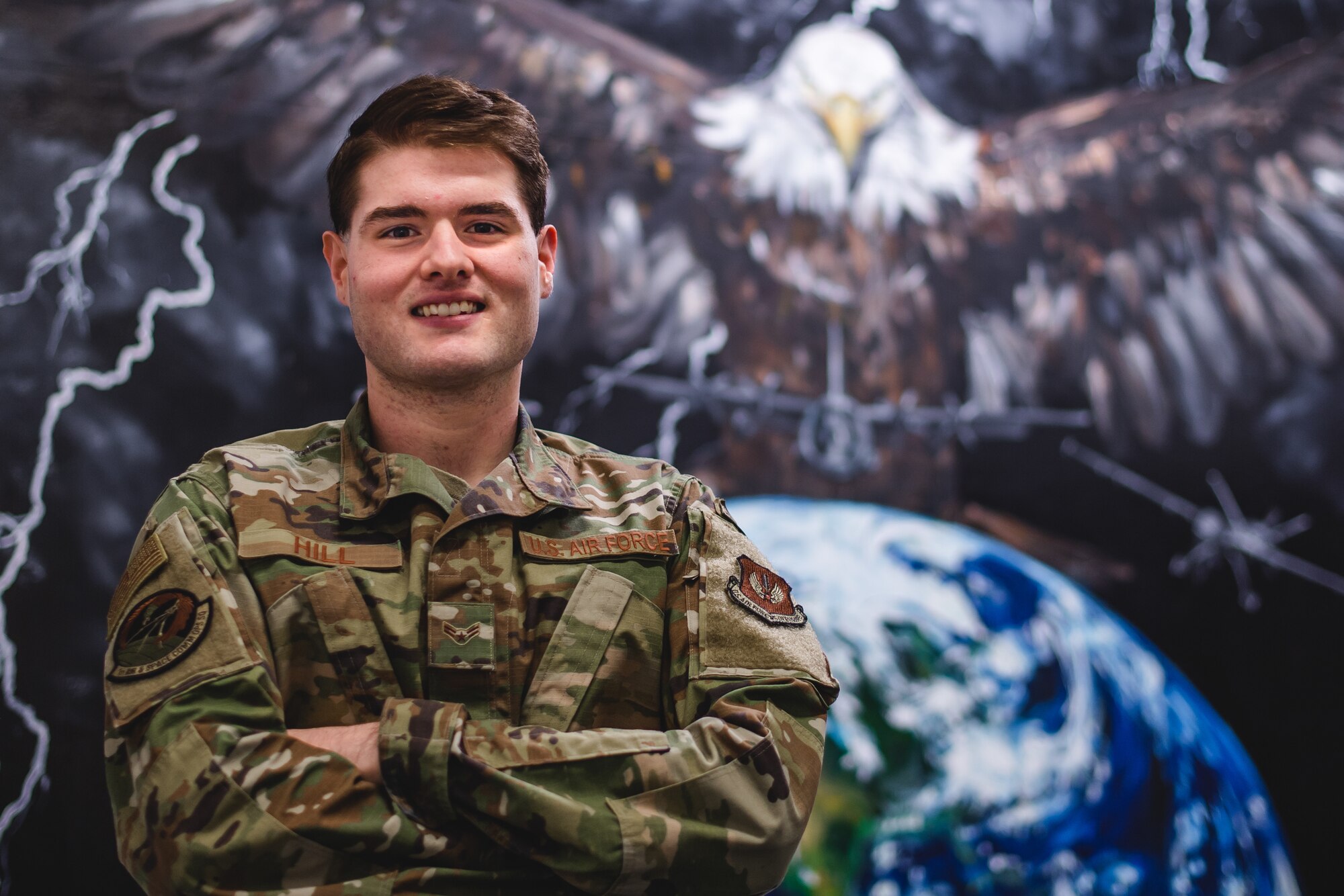 Photo of Airman posing in front of a mural depicting an Eagle over Earth