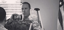 Air National Guard recruiter holds a phone showing a video display connecting an officer conducting the oath of enlistment with a new member