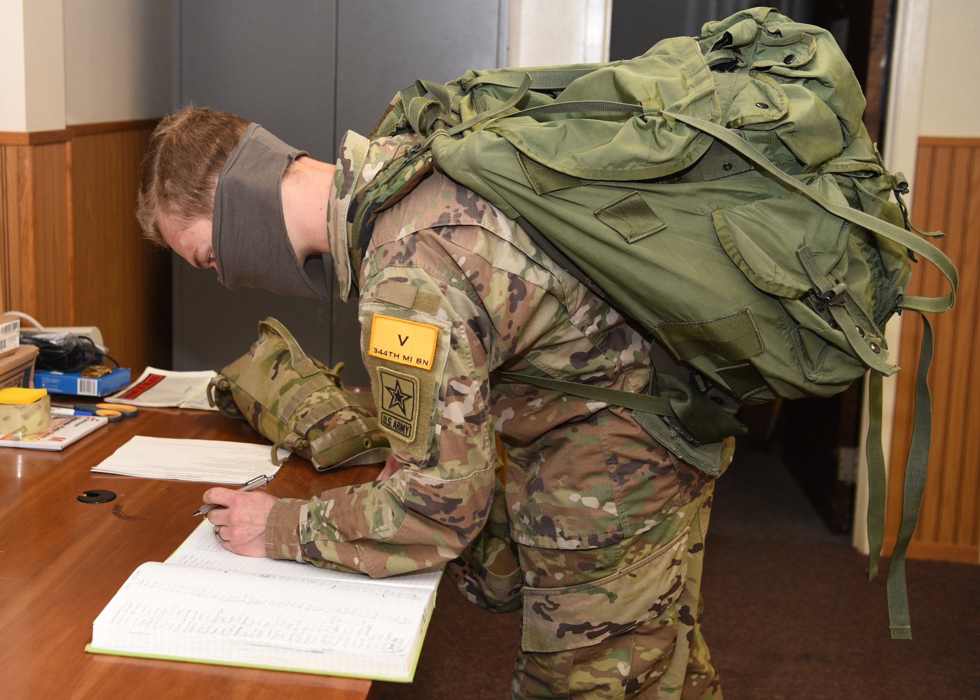 U.S. Army PV2 Collins Lee, 344th Military Intelligence Battalion student, signs a logistical copy log for equipment management while wearing a facemask. Lee practiced COVID-19 preventative measures through social distancing and wearing his mask.(U.S. Air Force photo by Airman 1st Class Abbey Rieves)