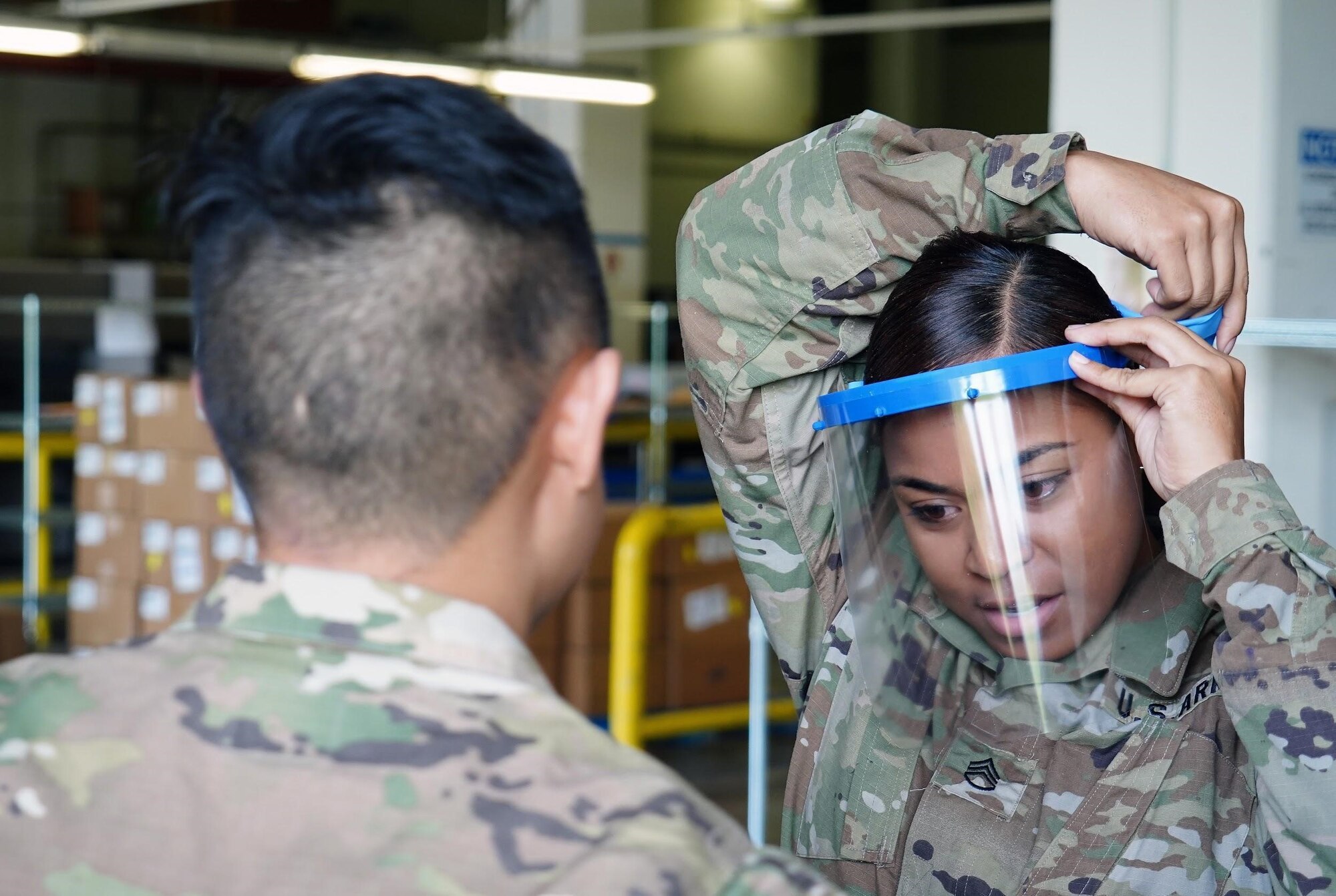 U.S. Army Capt. Scott Nguyen, Tripler Army Medical Center General Surgery resident physician, assists U.S. Army Staff Sgt. Jacklyn Smith, TAMC medical warehouse non-commissioned officer in charge, with adjusting her face shield at TAMC, Hawaii, April 3, 2020. Due to a shortage of disposable masks, the 15th Wing is using 3D printers to make face shields to donate across the island to combat the COVID-19 pandemic.  (U.S. Air Force photo by Airman 1st Class Erin Baxter)