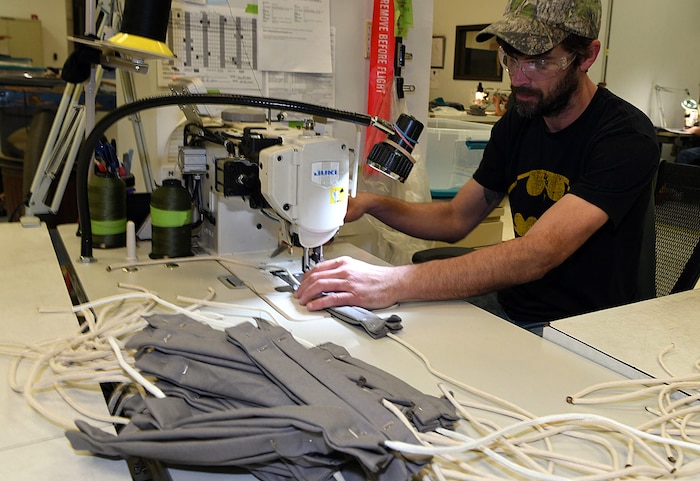 Photo shows a man sewing together a mask at a sewing machine.