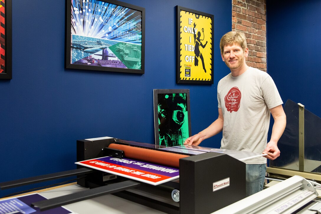Code 1170 Visual Information Specialist Eric MacLeod laminates and cuts a COVID-19 poster he designed.