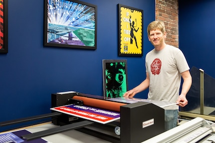 Code 1170 Visual Information Specialist Eric MacLeod laminates and cuts a COVID-19 poster he designed.