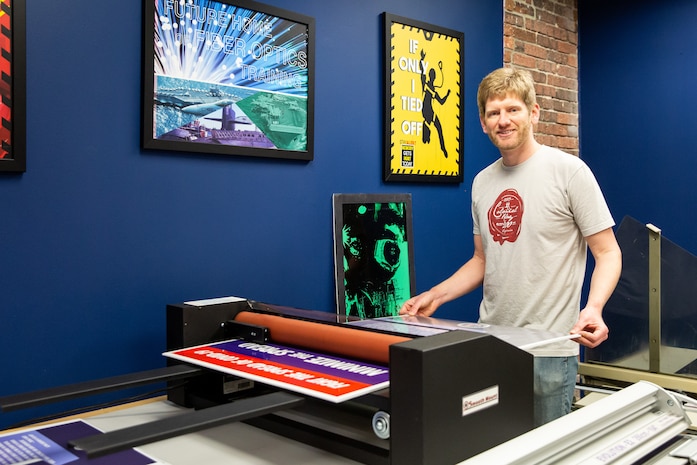 Code 1170 Visual Information Specialist Eric MacLeod laminates and cuts a COVID-19 poster he designed.