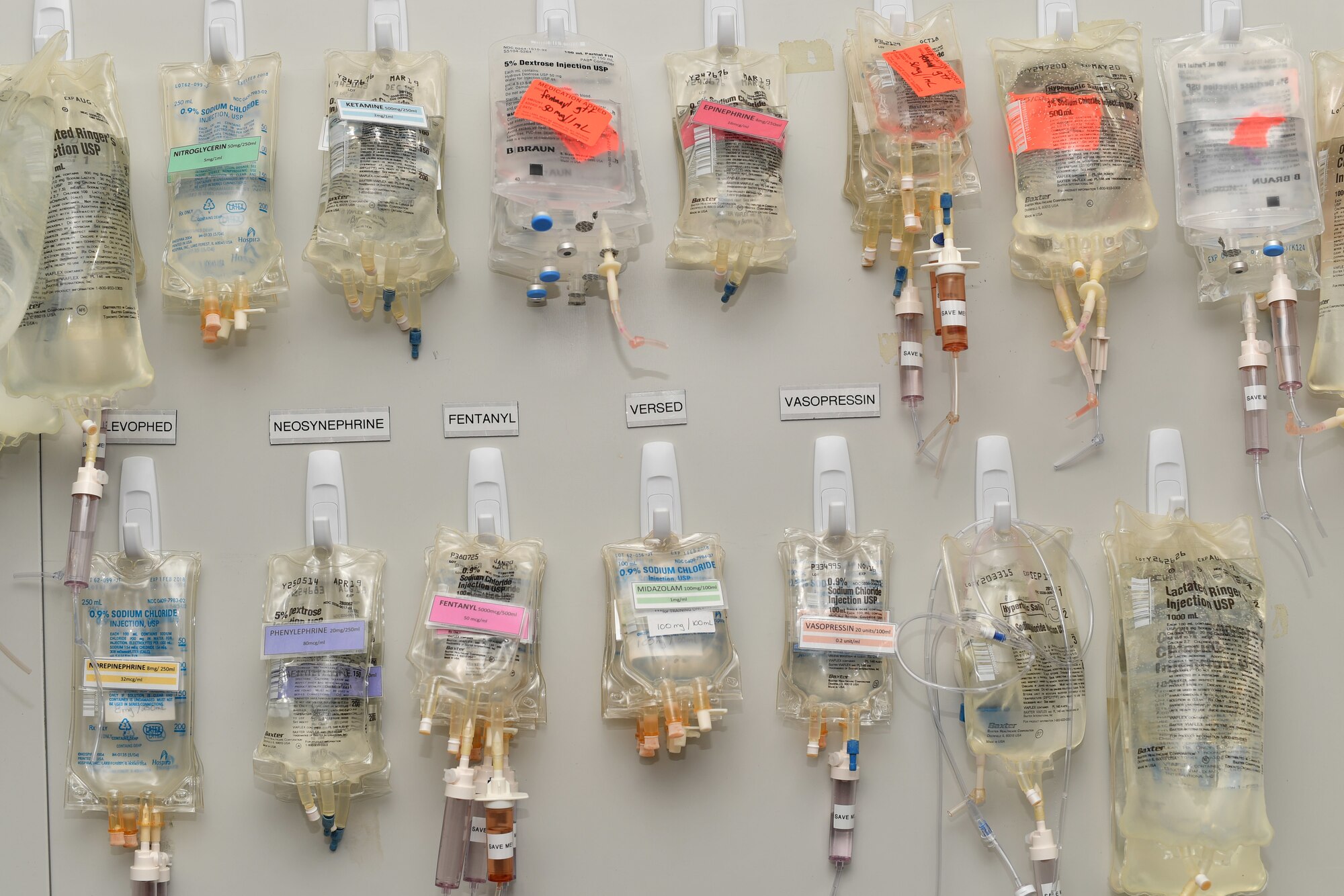 Medications in IV drip bags hang on a wall.
