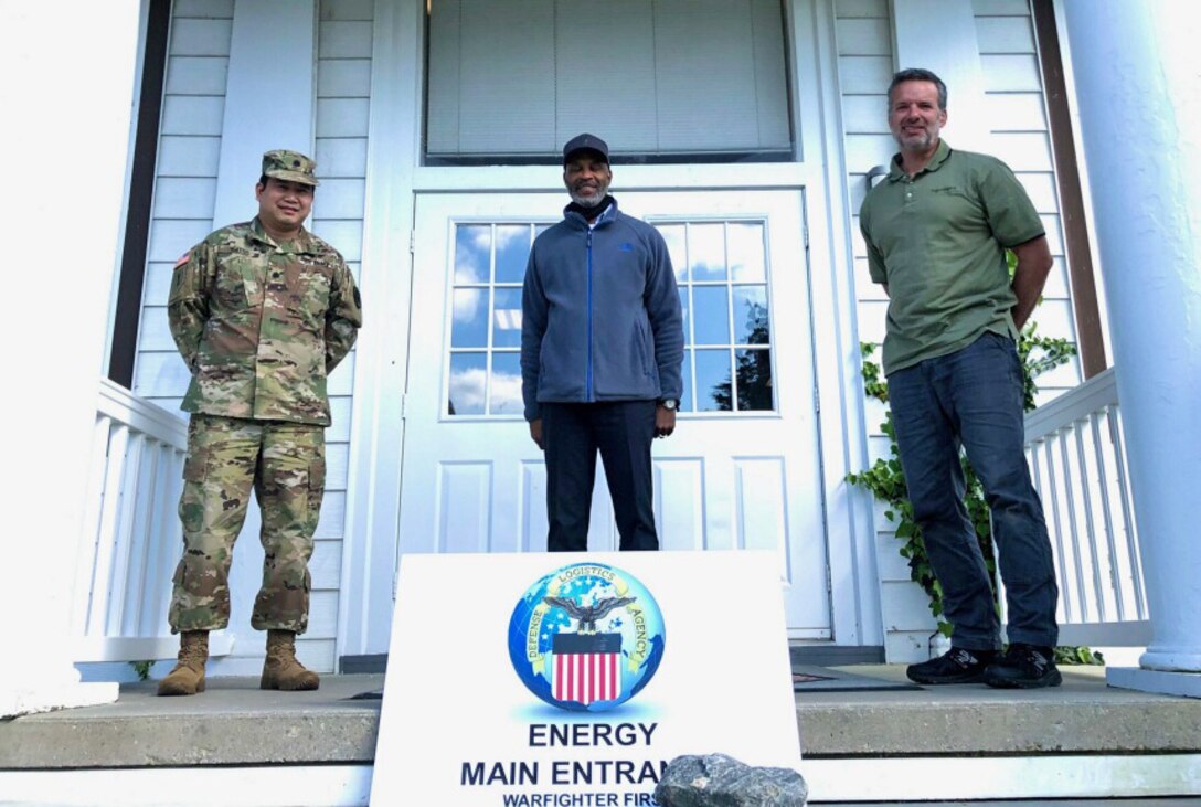 Three men, one in an Army uniform, stand on a porch