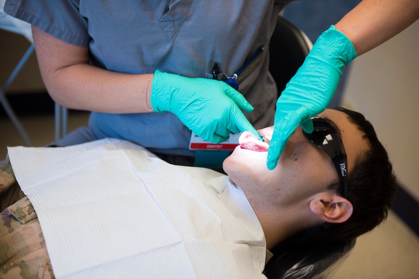 Maj. Leslie Chambers, a general dentist assigned to the 628th Operational Medical Readiness Squadron, performs a deployment exam on Senior Airman Garrett Ropon, an electrical power production journeyman assigned to the 628th Civil Engineering Squadron at Joint Base Charleston, S.C., April 21, 2020. The dental clinic is open for dental emergencies and deployment exams. Dental clinic personnel are protecting their patients and themselves by regularly cleaning surfaces, wearing masks and gloves, reducing the number of patients they see, practicing physical distancing whenever possible and having patients use pretreatment mouth rinse. (U.S. Air Force photo by Airman Sara Jenkins)