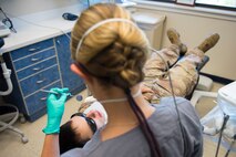 Maj. Leslie Chambers, a general dentist assigned to the 628th Operational Medical Readiness Squadron, performs a deployment exam on Senior Airman Garrett Ropon, an electrical power production journeyman assigned to the 628th Civil Engineering Squadron at Joint Base Charleston, S.C., April 21, 2020. The dental clinic is open for dental emergencies and deployment exams. Dental clinic personnel are protecting their patients and themselves by regularly cleaning surfaces, wearing masks and gloves, reducing the number of patients they see, practicing physical distancing whenever possible and having patients use pretreatment mouth rinse. (U.S. Air Force photo by Airman Sara Jenkins)