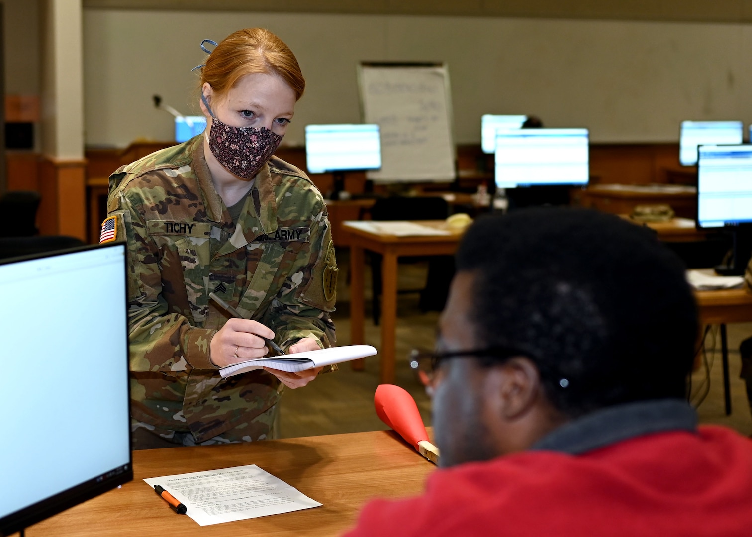 Sgt. Alexandria Tichy, a flutist with the 39th Army Band, New Hampshire Army National Guard, takes instructions from Kevin Myers, a civilian supervisor at an unemployment call center in Concord.
