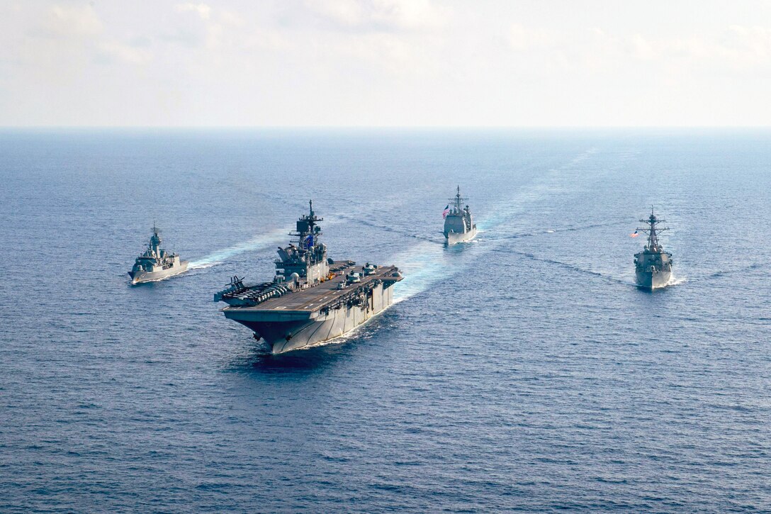 Four ships steam alongside each other on the ocean.