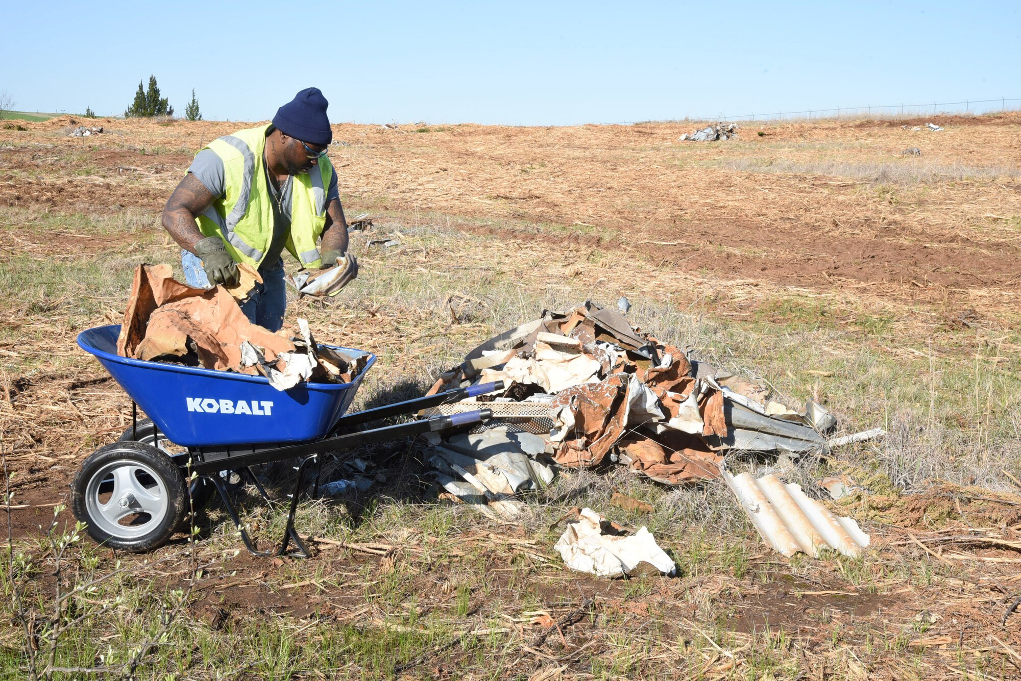 A worker with the Oklahoma City Metro Alliance's Firstep program fills a wheelbarrow with metal debris found littered throughout a 40-acre area outside of Tinker's southeast fenceline in an area deemed as a clear zone.