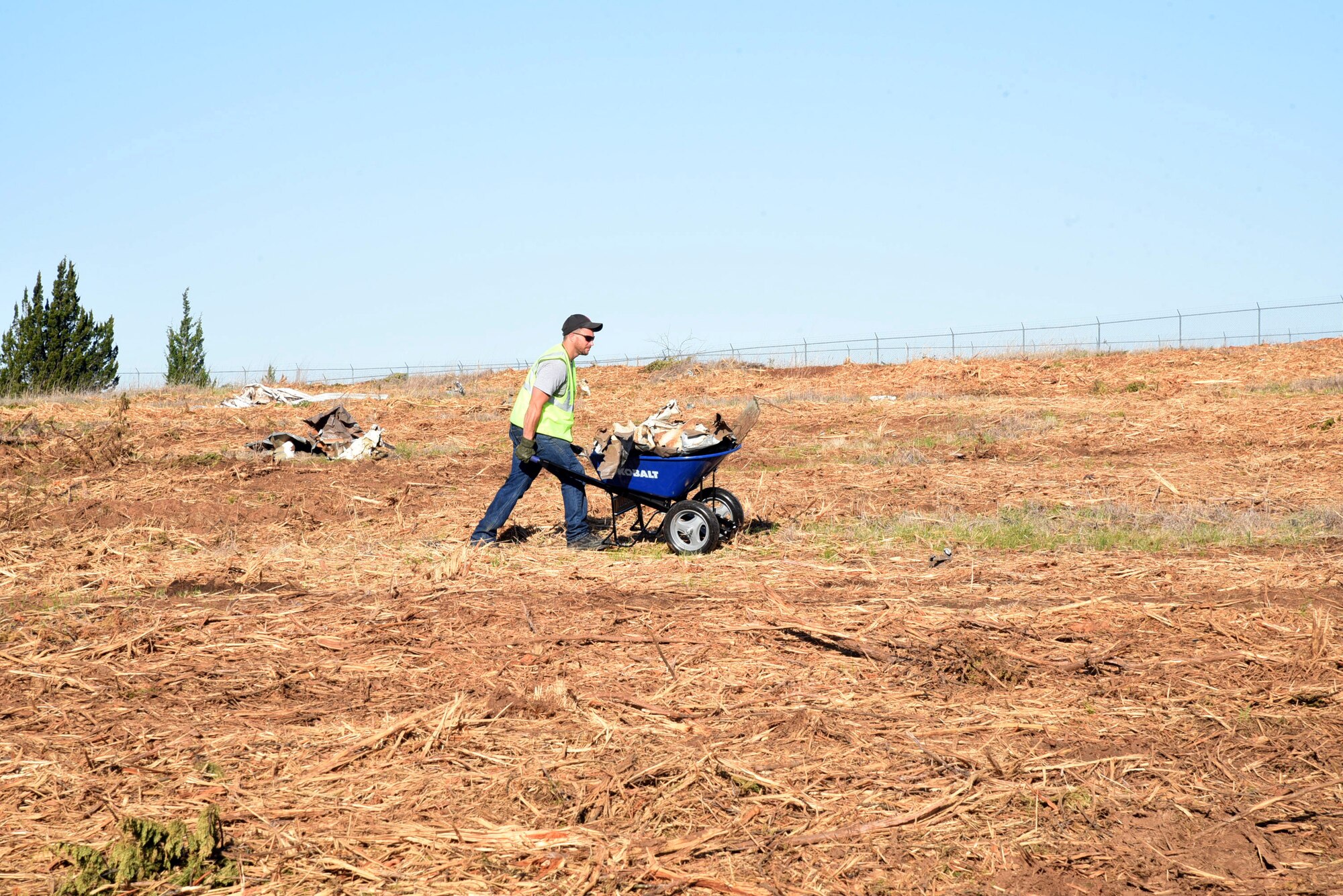 A worker with the Oklahoma City Metro Alliance's Firstep program fills a wheelbarrow with metal debris found littered throughout a 40-acre area outside of Tinker's southeast fenceline in an area deemed as a clear zone.