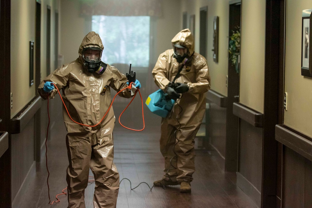 Two National Guardsmen wearing protective suits clean a hallway.