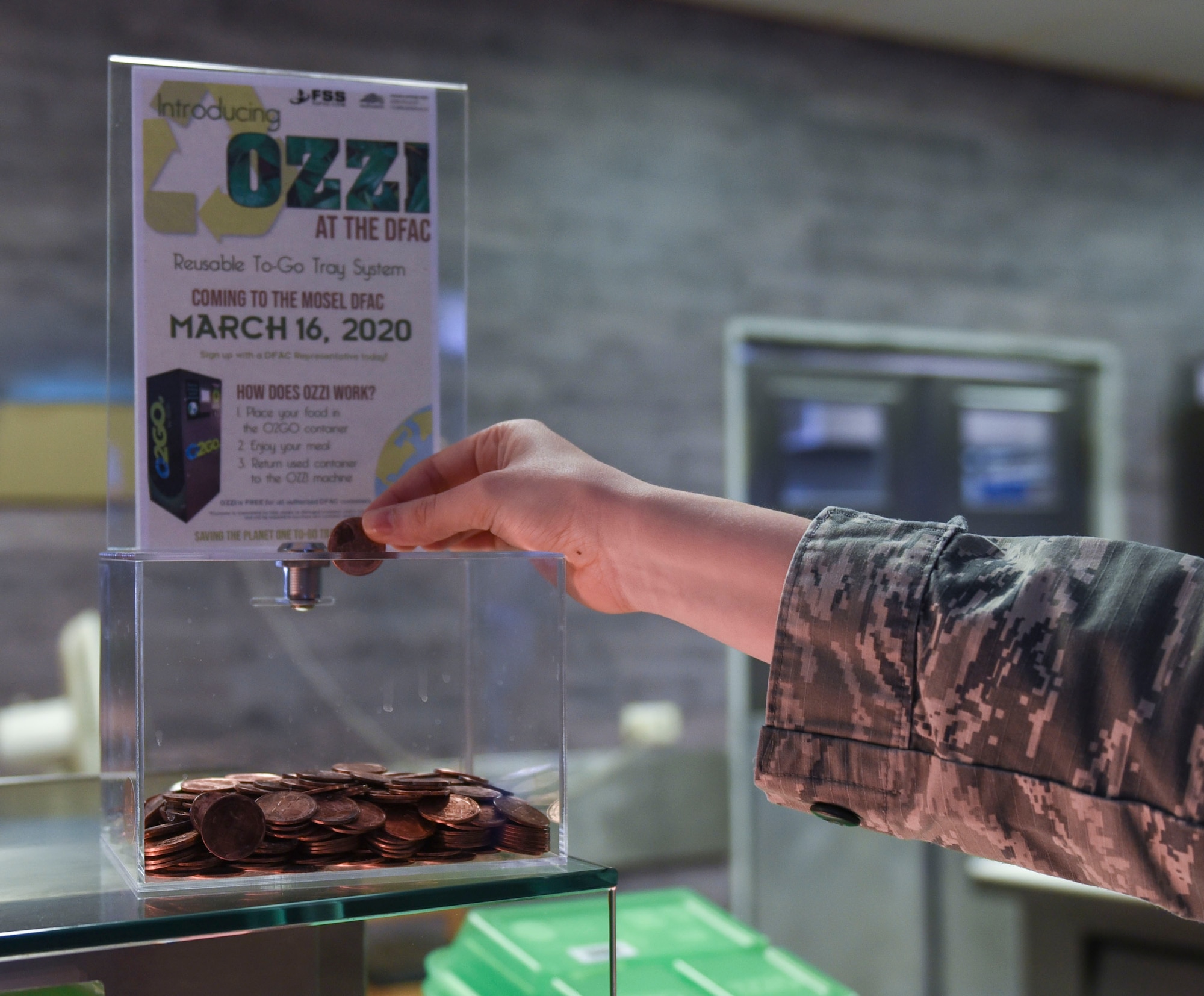 U.S. Air Force Airman 1st Class Leiah Copeland, 52nd Force Support Squadron food service journeyman, demonstrates where to put an OZZI token at Spangdahlem Air Base, Germany, April 20, 2020. OZZI meal trays save Spangdahlem AB $17,000 in funds, promotes recycling to Airmen and families, and helps the environment. (U.S. Air Force photo by Senior Airman Melody W. Howley)