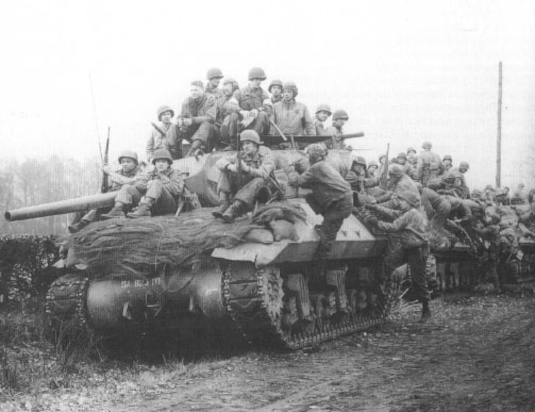 Several soldiers sit on top of three tanks.