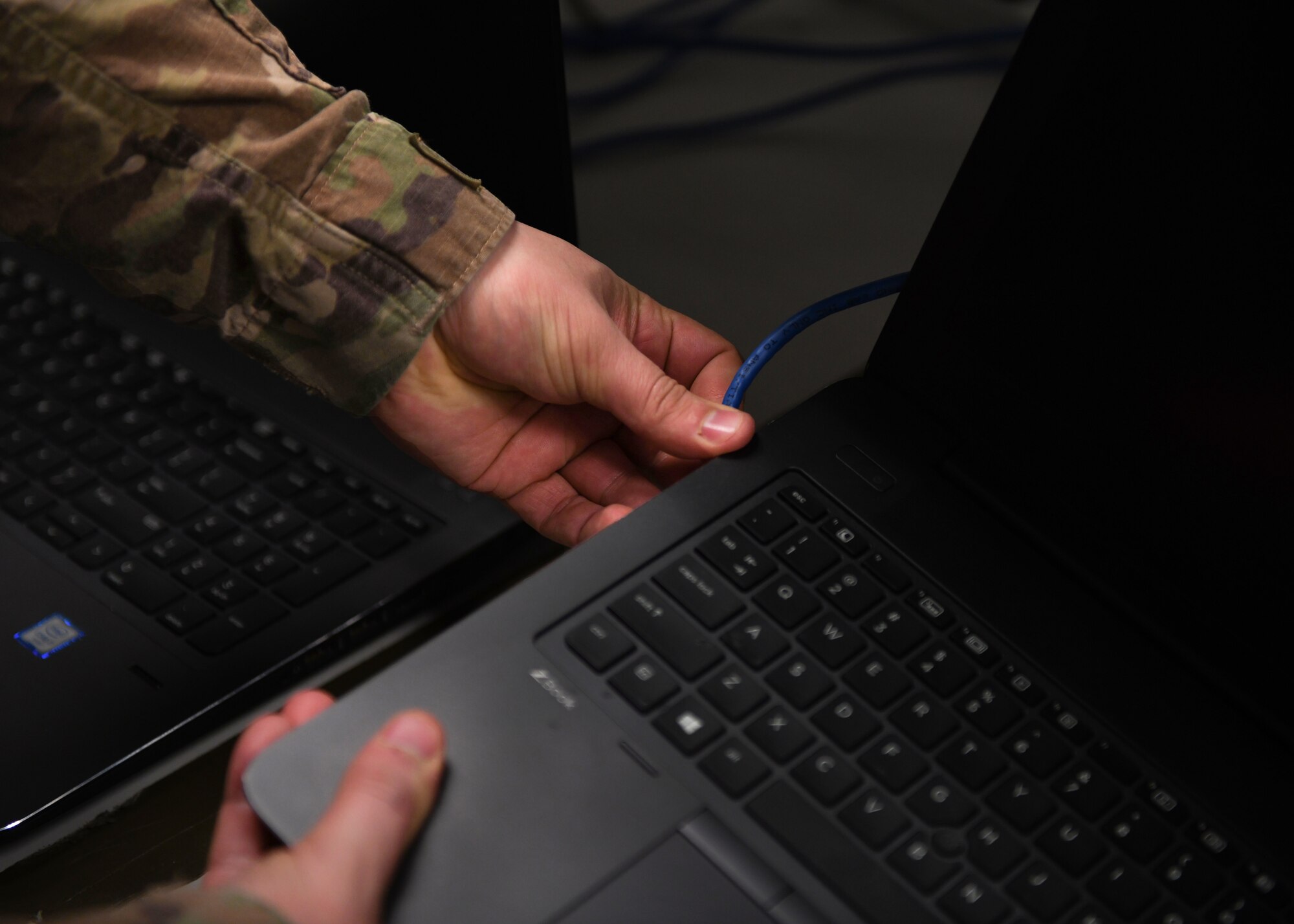 An Airman plugs a cable into a laptop.
