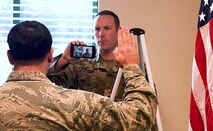 Air National Guard recruiter holds phone displaying video of recruit as an officer administers the oath of enlistment.