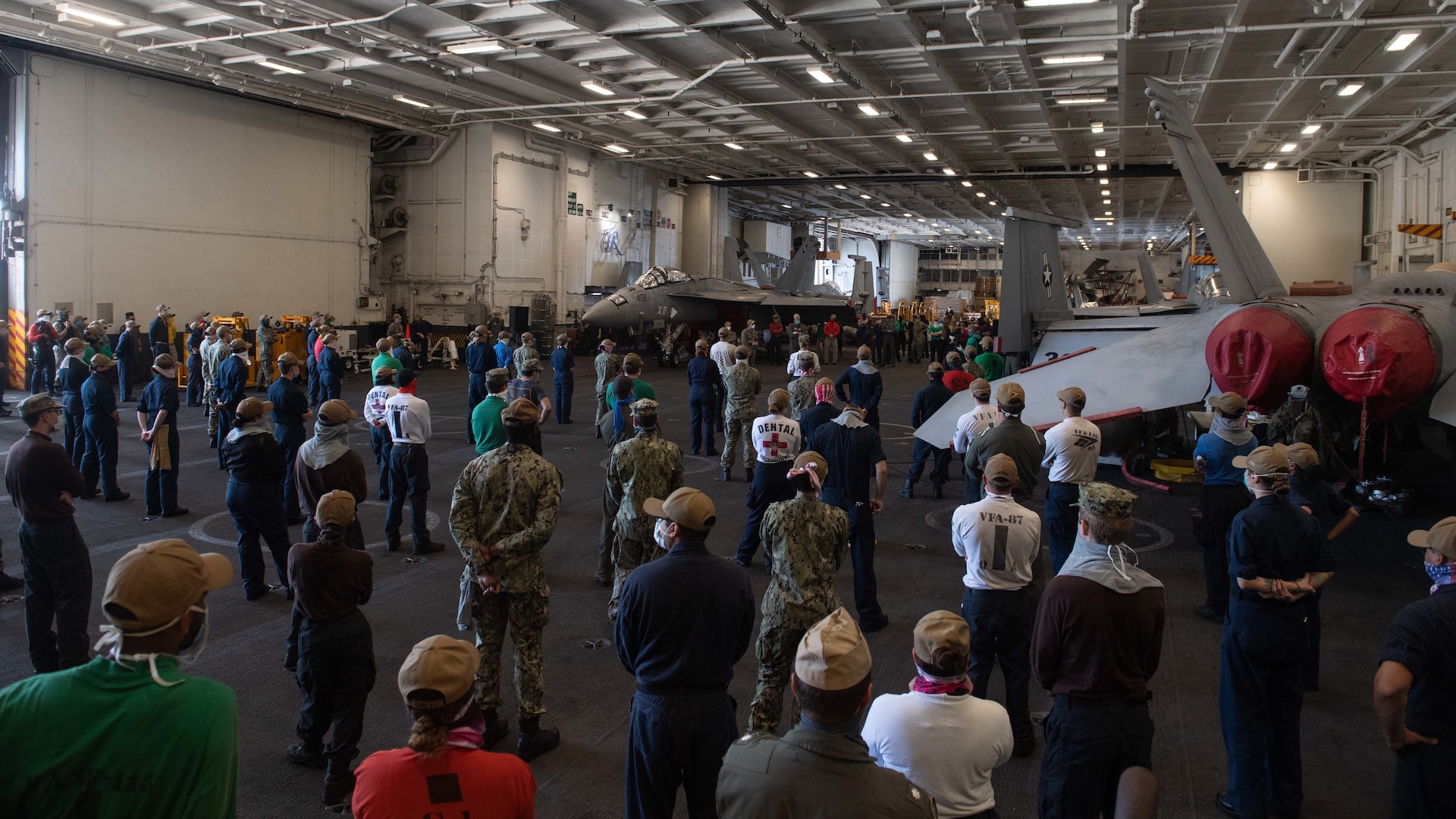 people standing in an aircraft bay listening to speaker