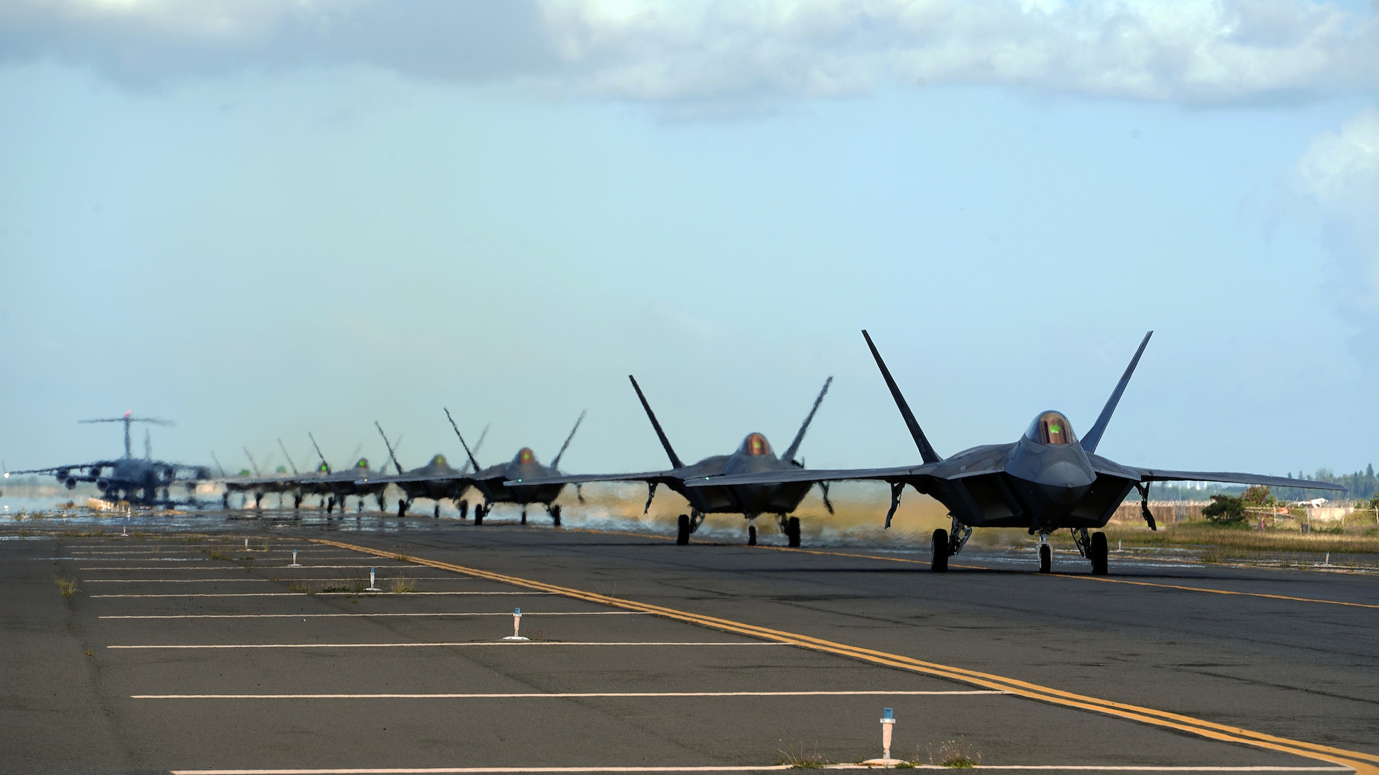 Eight U.S. Air Force F-22 Raptors, a KC-135 Stratotanker and a C-17 Globemaster III taxi on the runway during a routine training schedule April 21, 2020, at Honolulu International Airport, Hawaii. Given the low traffic at the airport due to COVID-19 mitigation efforts, the active-duty 15th Wing and the Hawaii Air National Guard’s 154th Wing seized an opportunity to document the operation which showcases readiness and their unique Total Force Integration construct. The units of Team Hickam work together seamlessly to deliver combat airpower, tanker fuel, and humanitarian support and disaster relief across the Indo-Pacific. (U.S. Air Force photo by Airman 1st Class Erin Baxter)