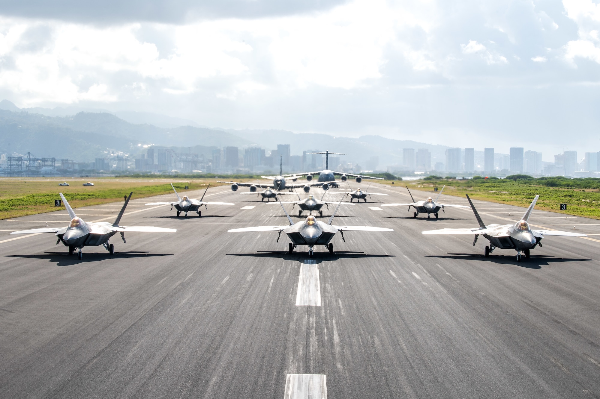 Eight U.S. Air Force F-22 Raptors, a KC-135 Stratotanker and a C-17 Globemaster III taxi on the runway during a routine training schedule April 21, 2020, at Honolulu International Airport, Hawaii. Given the low traffic at the airport due to COVID-19 mitigation efforts, the active-duty 15th Wing and the Hawaii Air National Guard’s 154th Wing seized an opportunity to document the operation which showcases readiness and their unique Total Force Integration construct. The units of Team Hickam work together seamlessly to deliver combat airpower, tanker fuel, and humanitarian support and disaster relief across the Indo-Pacific. (U.S. Air National Guard photo by Senior Airman John Linzmeier)