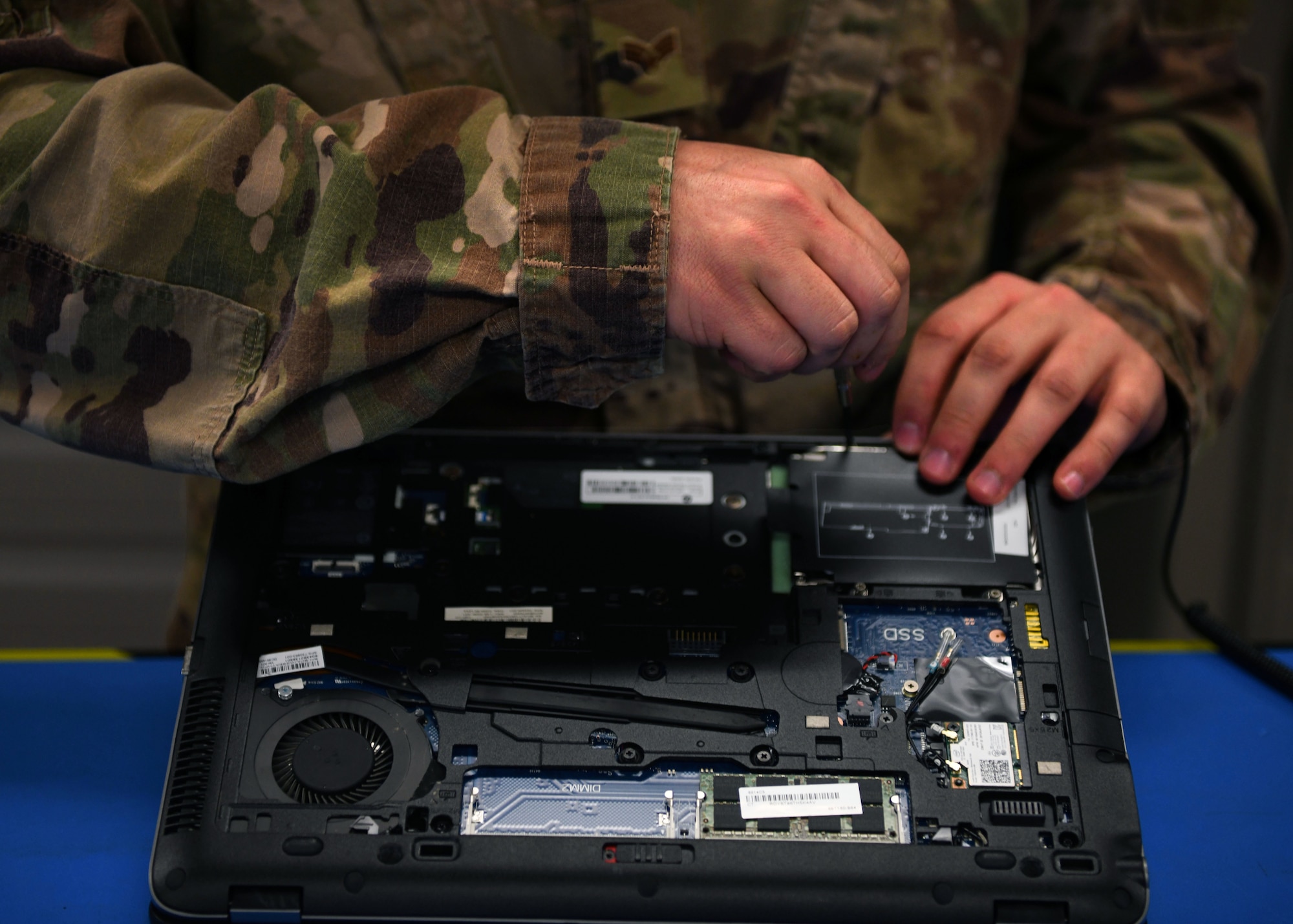 An Airman removes a screw from a laptop.