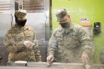 Staff Sgt. Shelona Dudley, (left) a food service journeyman assigned to the 628th Force Support Squadron supervises Airman 1st Class David Vecchione, also a food service journeyman assigned to the 628th Force Support Squadron, as he prepares food at the Gaylor Dining Facility at Joint Base Charleston, S.C., April 22, 2020. Dining facility personnel are cleaning more often, wearing masks and gloves and practicing physical distancing in order to protect themselves and customers. The DFAC is currently open for carry out only.