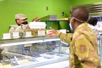 Senior Airman Jeremiah Jackson, a food service journeyman assigned to the 628th Force Support Squadron, hands food to a customer at the Gaylor Dining Facility at Joint Base Charleston, S.C., April 22, 2020. Dining facility personnel are cleaning more often, wearing masks and gloves and practicing physical distancing in order to protect themselves and customers. The DFAC is currently open for carry out only.