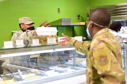 Senior Airman Jeremiah Jackson, a food service journeyman assigned to the 628th Force Support Squadron, hands food to a customer at the Gaylor Dining Facility at Joint Base Charleston, S.C., April 22, 2020. Dining facility personnel are cleaning more often, wearing masks and gloves and practicing physical distancing in order to protect themselves and customers. The DFAC is currently open for carry out only.