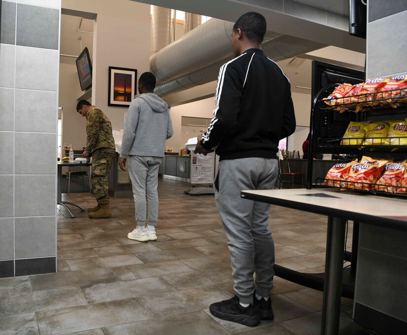 Airmen stand in line while observing social distancing at the Freedom Hall Airmen Dining Facility on Joint Base Andrews, Md., Apr. 7, 2020. The DFAC has placed lines of tape on the ground spaced six feet apart in order to help maintain the social distancing requirements. (U.S. Air Force photo by Airman 1st Class Spencer Slocum)
