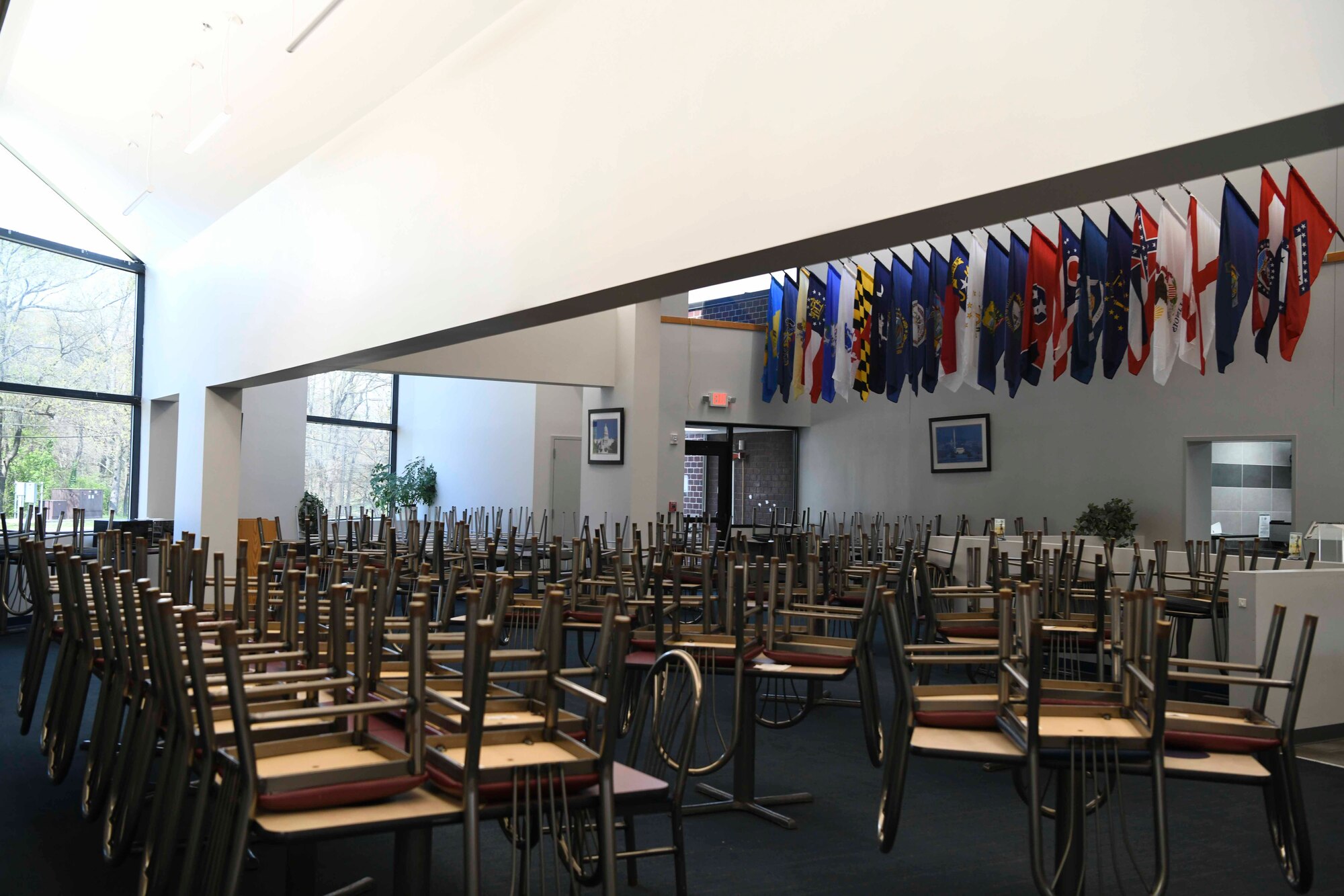 Chairs rest upside-down on the tops of tables at the Freedom Hall Airmen Dining Facility on Joint Base Andrews, Md. Apr. 7, 2020. In an effort to reduce the spread of COVID-19, meals are carry-out only, and the building is cleaned consistently throughout the day. (U.S. Air Force photo by Airman 1st Class Spencer Slocum)
