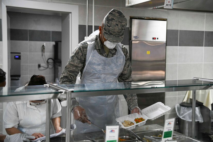 Senior Airman Samuel Airahuobhor, 11th Force Support Squadron services line server, scoops food into a container at the Freedom Hall Airmen Dining Facility on Joint Base Andrews, Md. Apr. 7, 2020. If an Airmen is unable to pick up their food during COVID-19, they may have someone else come and pick up their food for them. (U.S. Air Force photo by Airman 1st Class Spencer Slocum)
