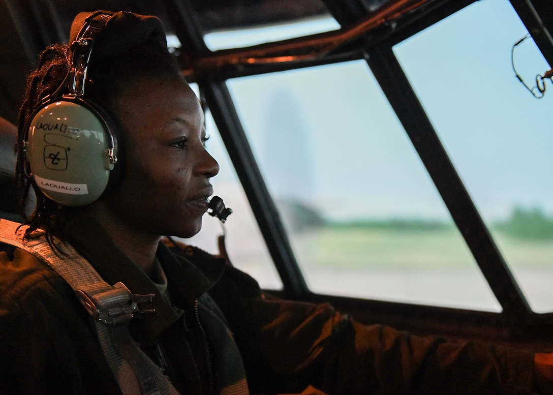 A woman siting in the pilot seat of a C-130 simulator.