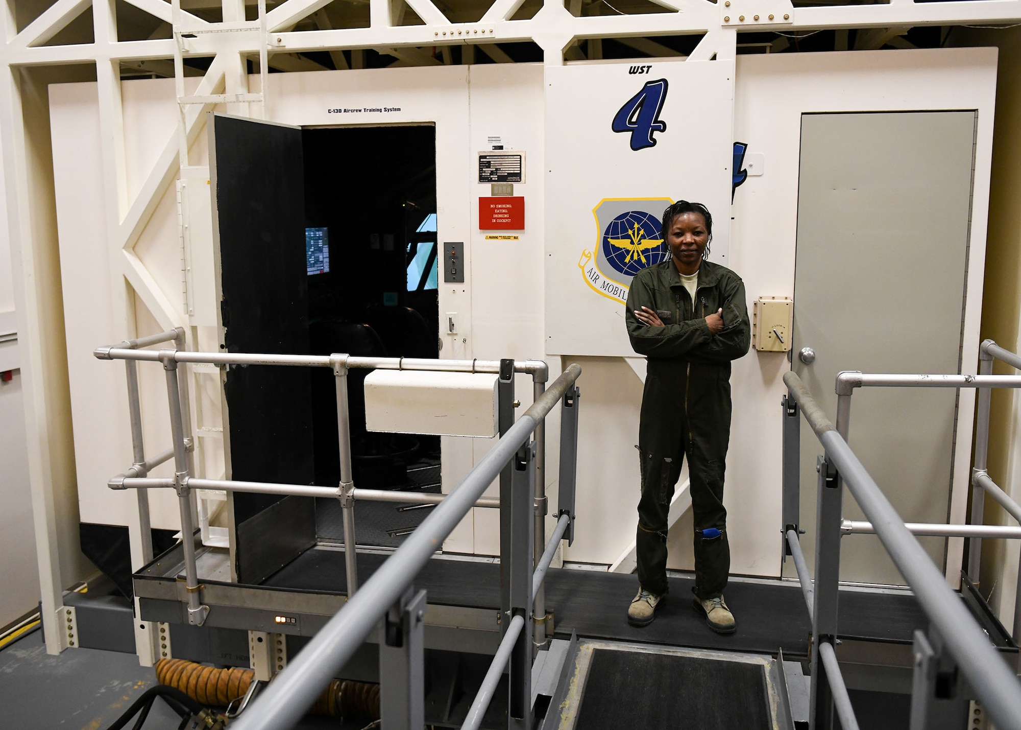 A woman stands in front of a C-130 simulator.
