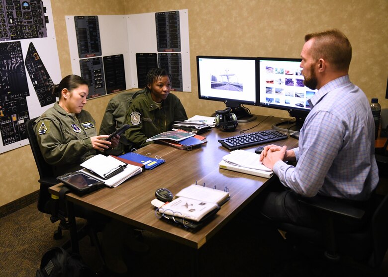 3 people sit a desk and have a conversation.