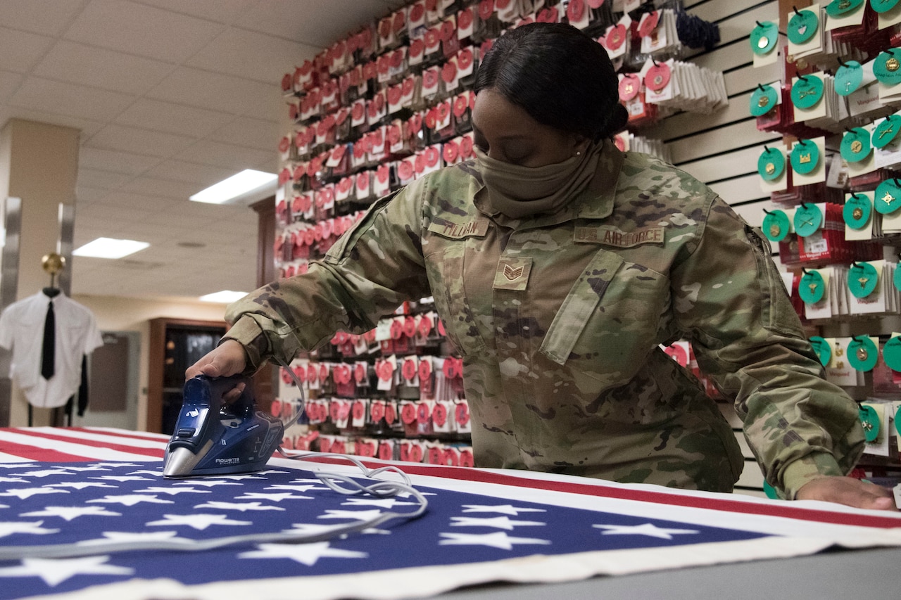 An airman irons an American flag.