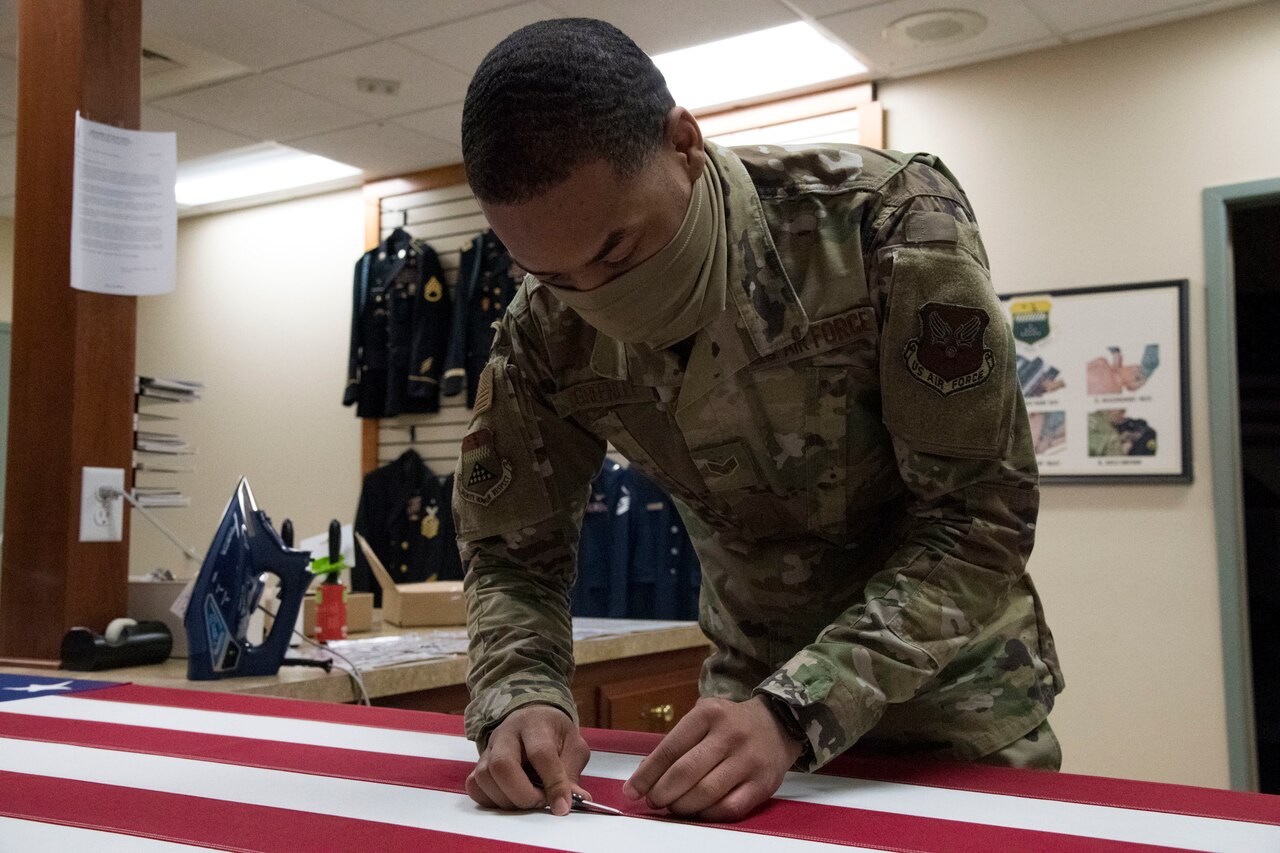 An airman trims a loose thread from an American flag.