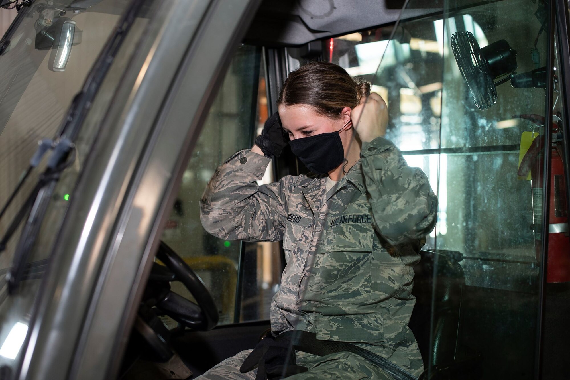 A female Airman in a forklift dons a black face mask inside of a warehouse