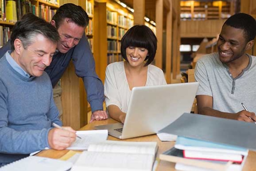 Three men and a woman huddle around a laptop computer.