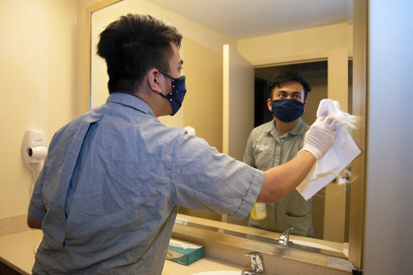 Jether Velasquez, Presidential Inn housekeeper, wipes down a bathroom mirror in a Temporary Lodging Facility room on Joint Base Andrews, Md., April 13, 2020. Velasquez wears a mask and gloves to reduce potentially being exposed to the coronavirus disease.