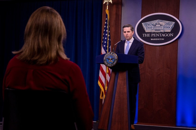 A man stands at a lectern and talks to a woman who is seen from the back.