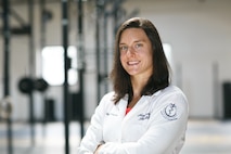 white female with brown hair stands with arms crossed in a medical jacket.