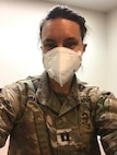 white female with brown hair in green camouflage uniform and white face mask.